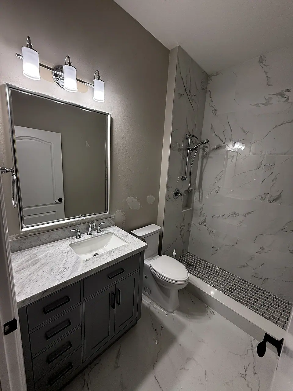 Bath with a grey shaker vanity, marble-look tile and a walk-in shower