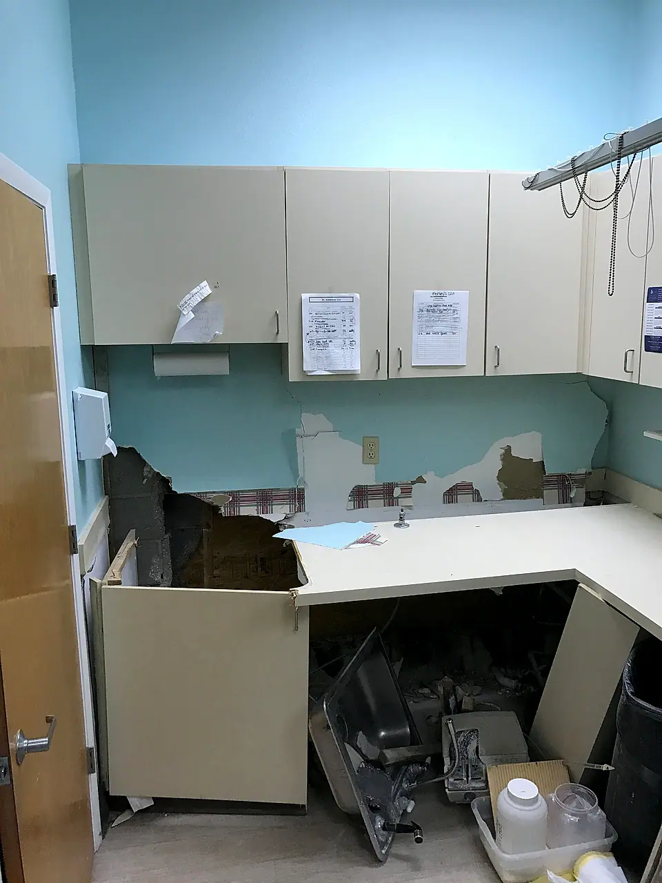 Water-damaged office break room with the lower cabinets torn open and the countertop gone