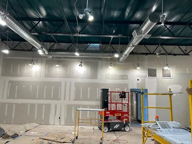 Commercial space with drywall finished, scaffolds and a lift, under exposed ductwork