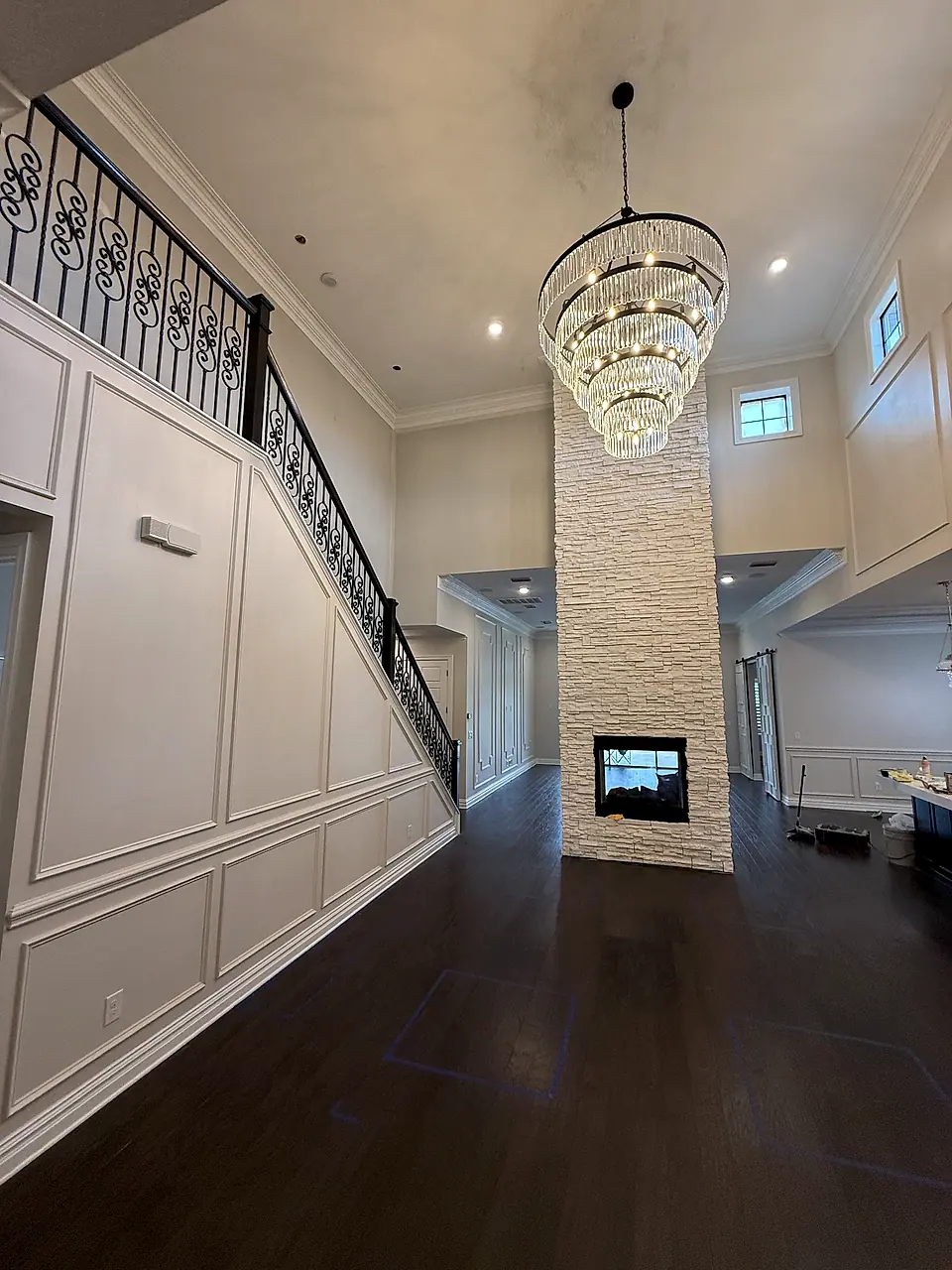 Two-story foyer with wainscoting, a stone fireplace column and a crystal chandelier