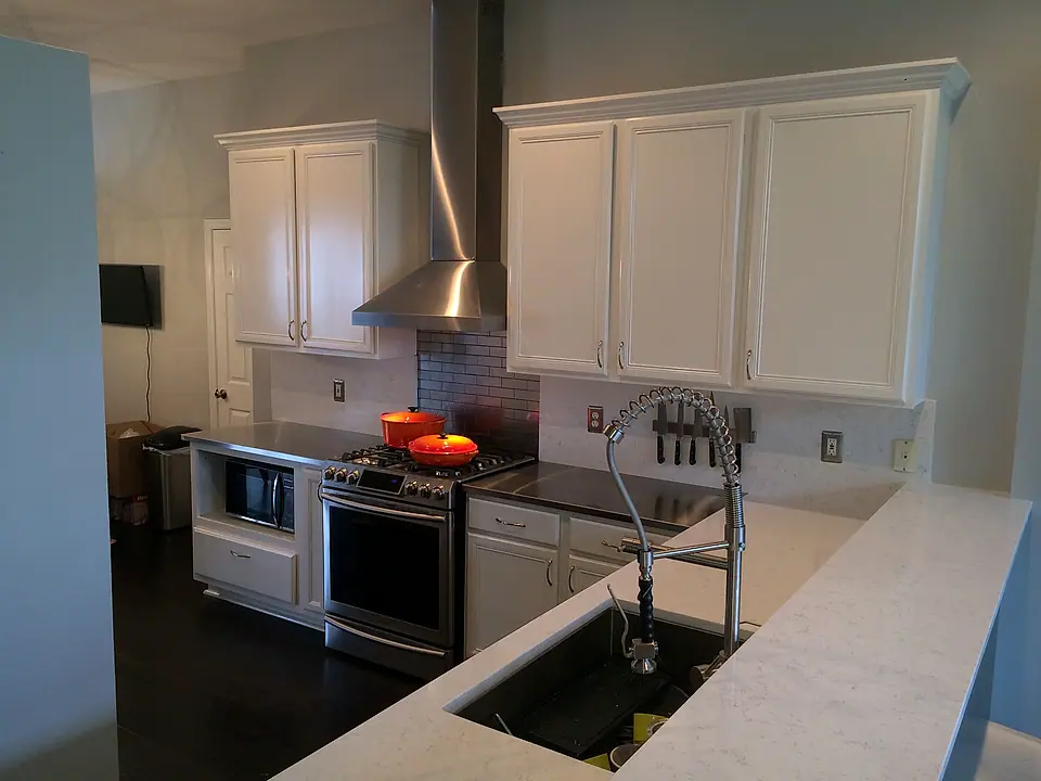 White shaker kitchen with a stainless range hood, marble-look counters and an undermount sink