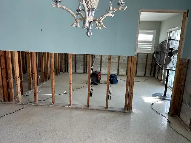 Water-damaged wall cut out to the studs with drying equipment and a fan