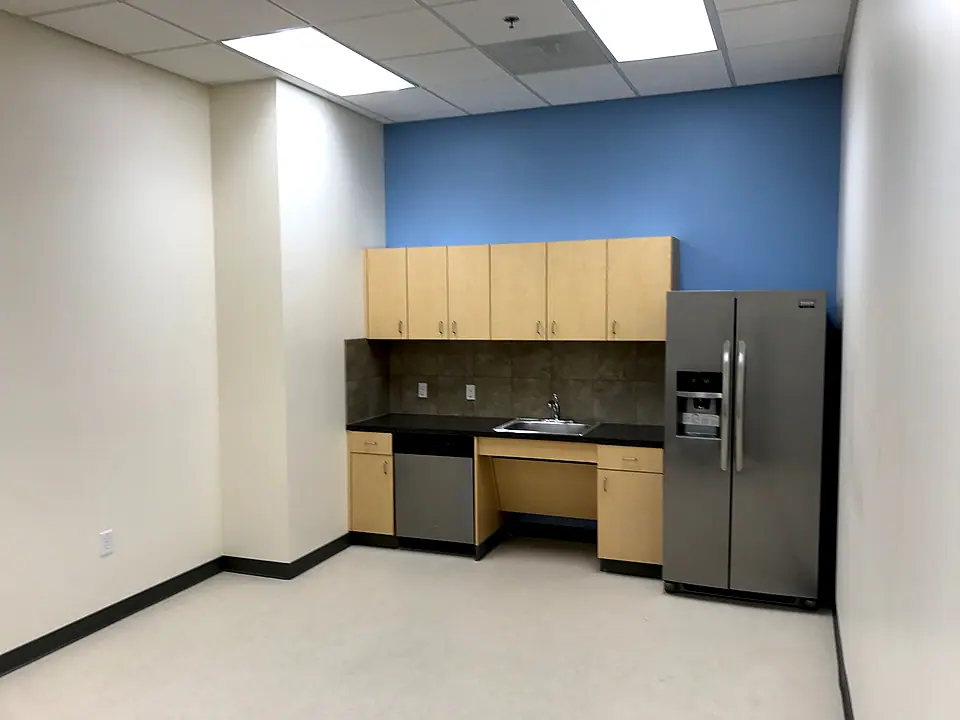 Office kitchenette build-out with maple cabinets, dark counters and a stainless refrigerator