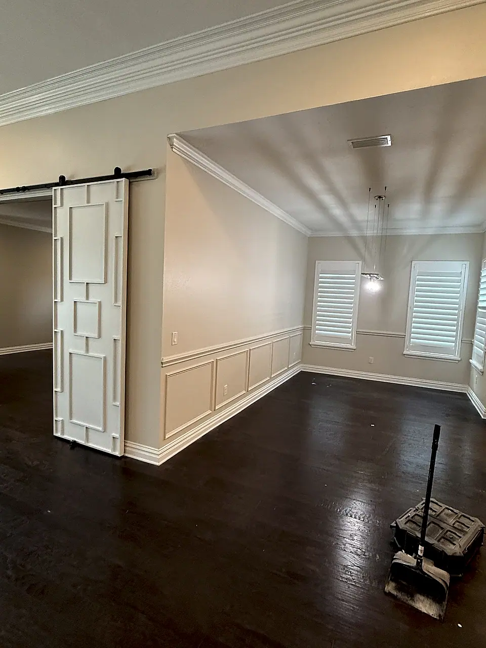 Room with a barn door, crown molding, wainscoting and dark hardwood floors