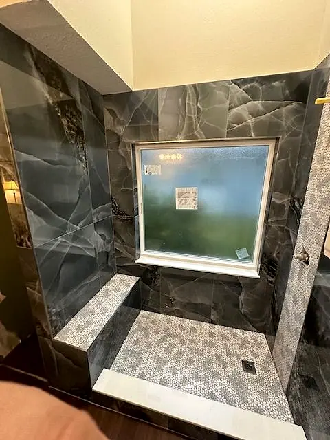 Walk-in shower with dark marble-look walls, a tiled bench and a window