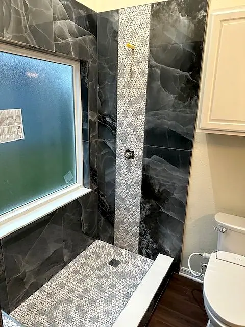 Shower with dark marble-look tile and a patterned mosaic accent stripe