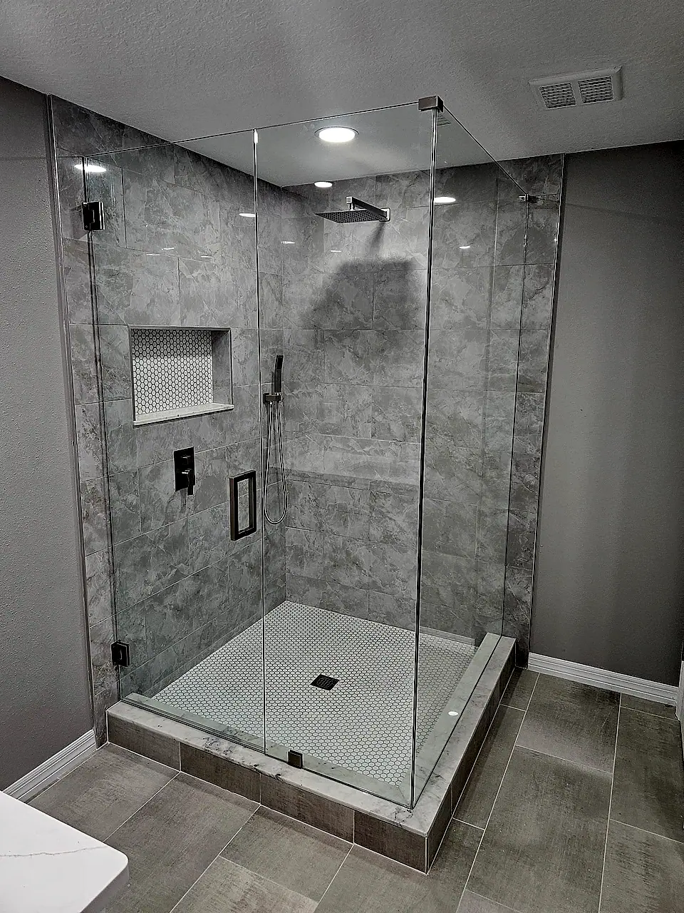 Frameless glass corner shower with large-format grey tile, rain head and recessed niche