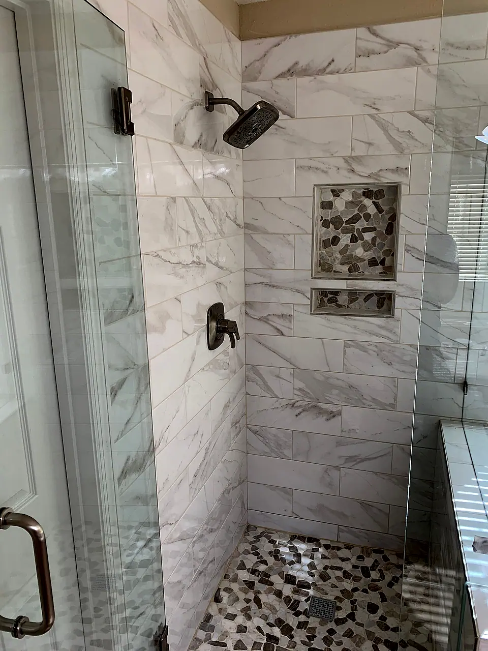 Walk-in shower with marble-look subway tile, a pebble floor and bronze fixtures