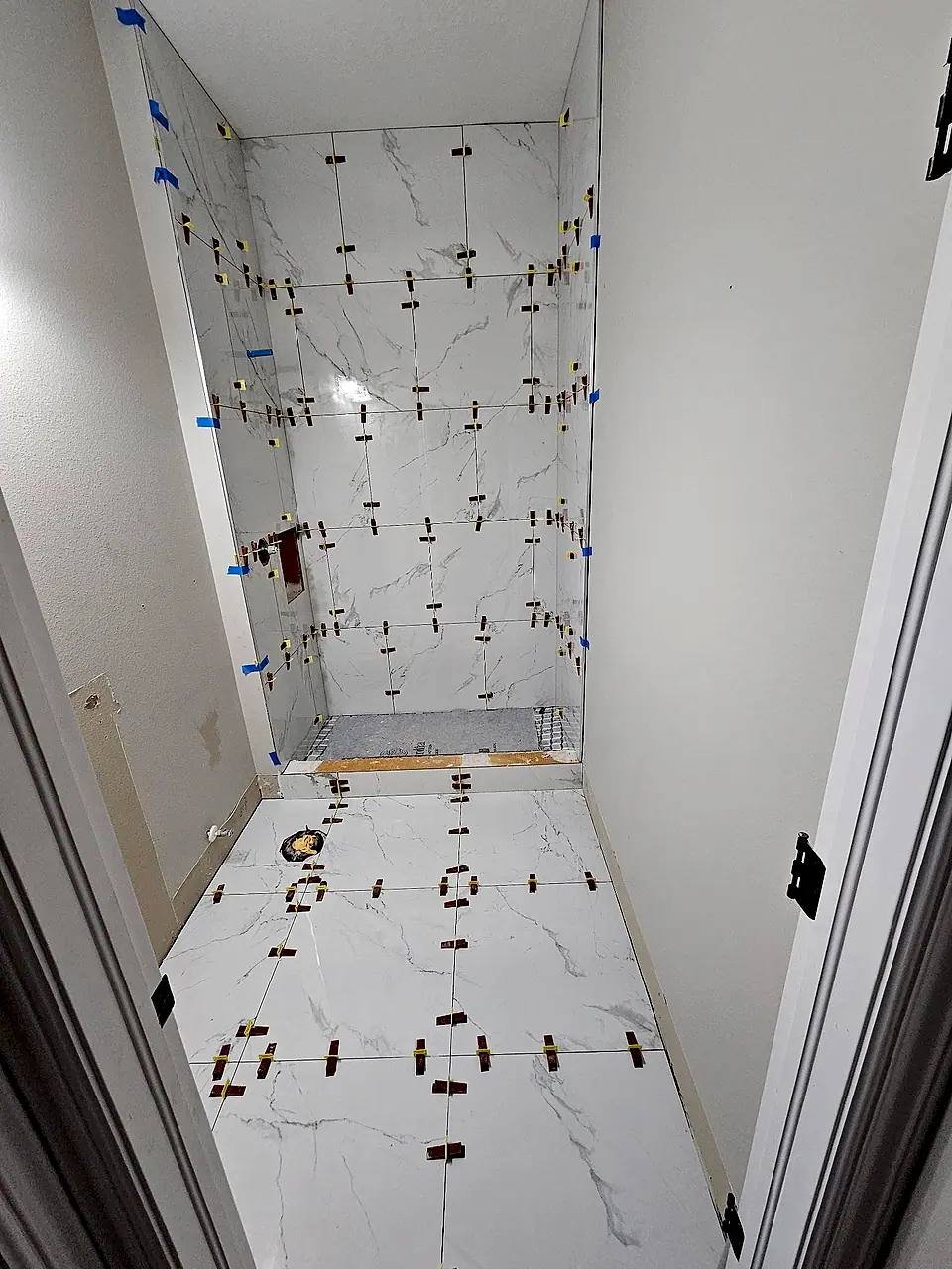 Marble-look porcelain tile going up with leveling clips in a walk-in shower