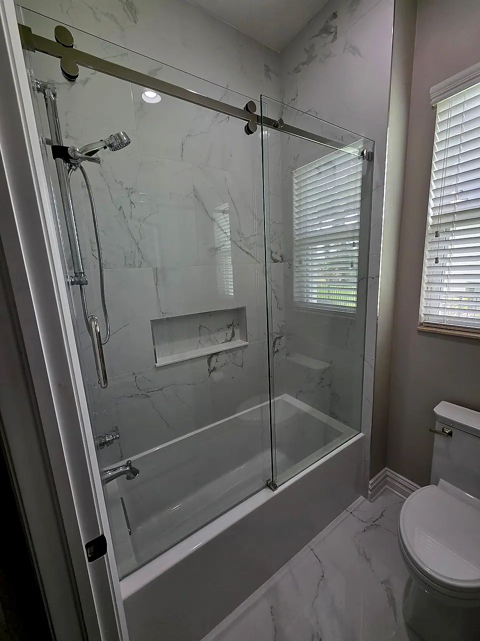 Tub and shower with a sliding glass door and marble-look wall tile